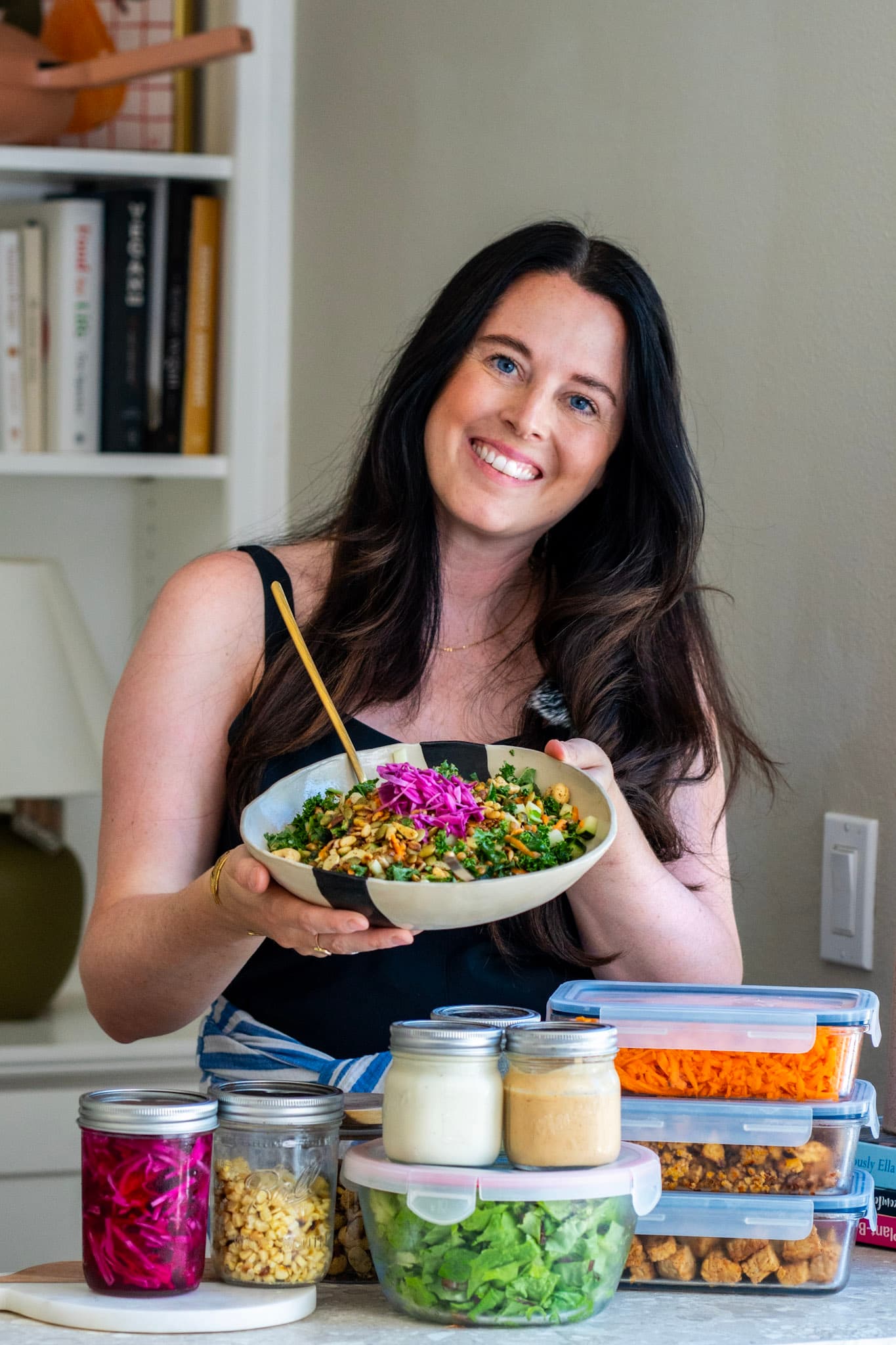 Eva holding a finished grain bowl behind a counter of prepped ingredients