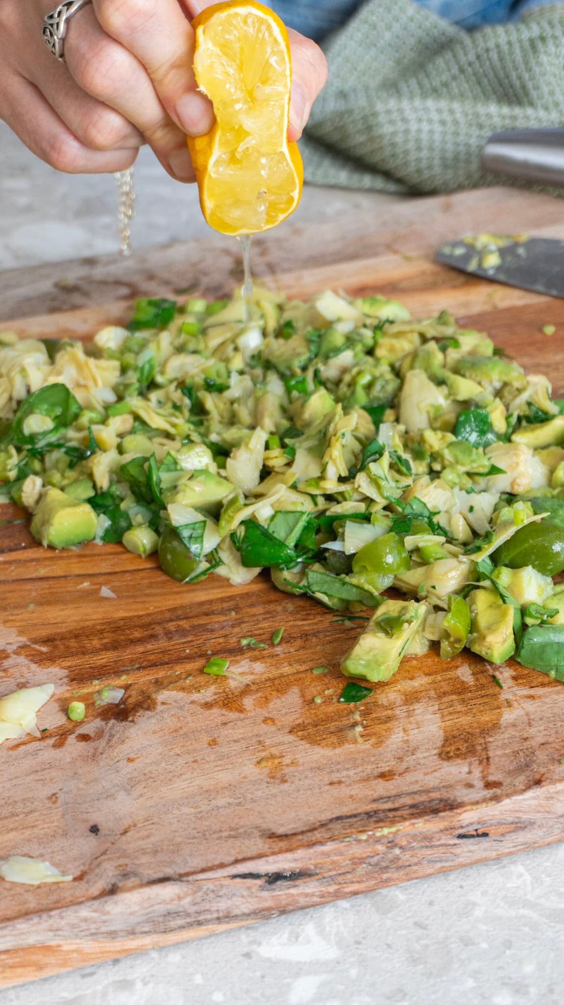 Lemon being squeezed over chopped brussels sprouts, avocado and herbs on a wooden board