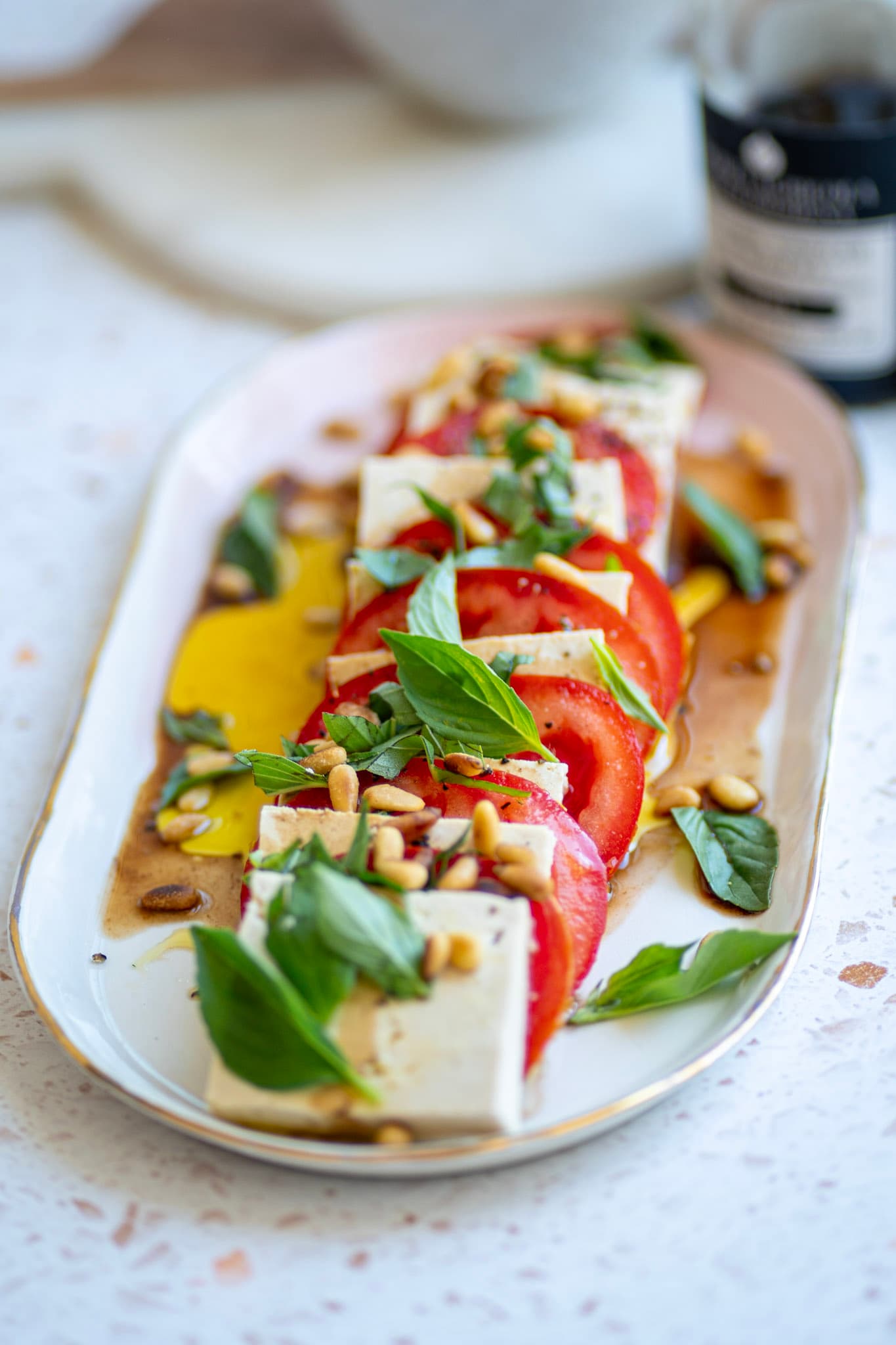 Sliced tomato and feta caprese with basil and pine nuts on a gold-rimmed platter